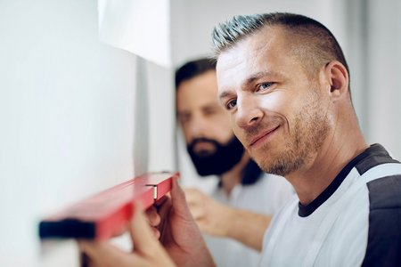 Arbeiter richtet rote Wasserwaage an glatter Wand aus